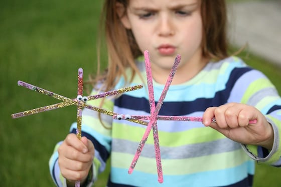 child playing with 2 dragonflies made from wooden stir sticks