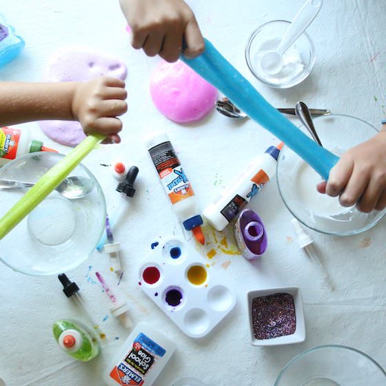 kids stretching Elmer's glue slime over table of slime ingredients