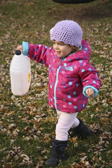 toddler carrying milk jug bird feeder to the back of the yard