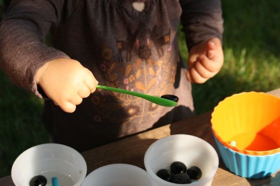 toddler scooping black beads with small green spoon 