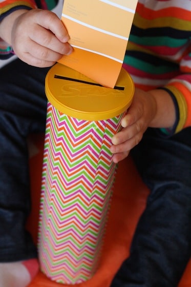 toddler dropping paint swatches through slit in pringles can lid