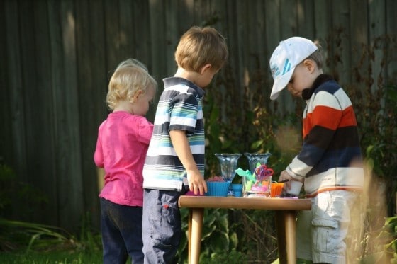 toddler and preschoolers gathered around play dough table in backyard