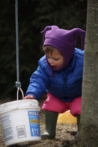 toddler investigating plastic bucket with top tied to handle