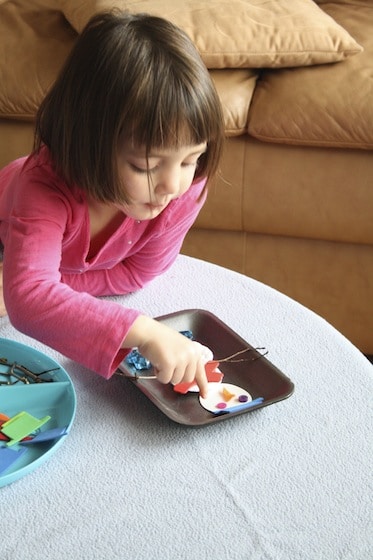 child building a snowman on a table top with craft scraps