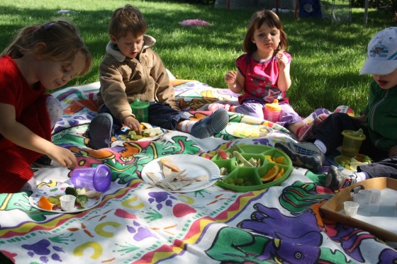 toddler and preschoolers having lunch on blanket under tree