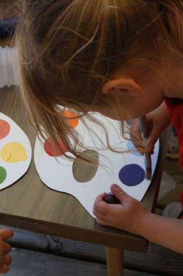 preschooler dipping paintbrush in purple paint on pretend paint palette