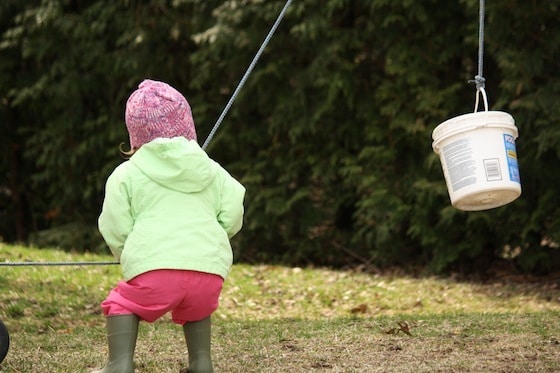 toddler hoisting a bucket with rope