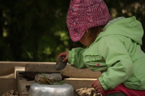 toddler putting stones in bowl in sandbox