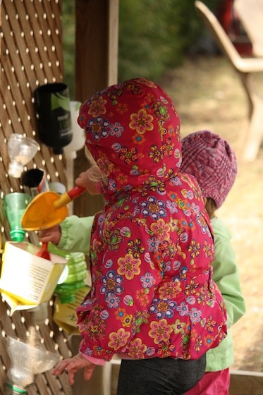 toddlers shovelling sand into containers on sand wall