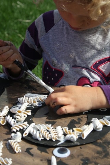 toddler gluing dried pasta to halloween wreath