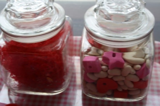 glass jars filled with small red, pink and white items for toddlers to examine