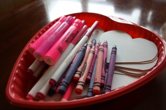 red plastic heart shaped tray with crayons markers and white cardboard hearts