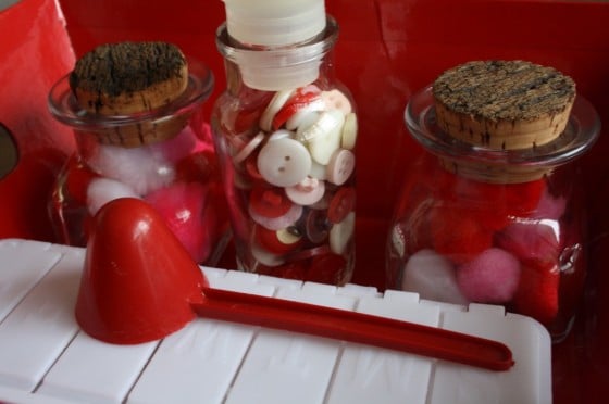 glass jars filled red, white and pink buttons, pom poms and beads, red scoop