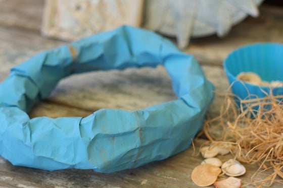 blue paper bag rolled into mermaid crown beside shells and raffia