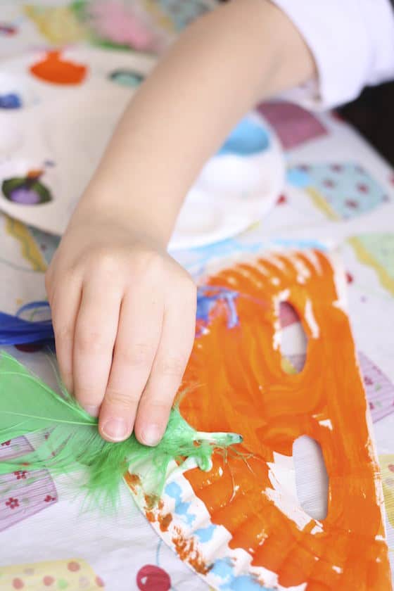 gluing craft feathers onto a paper plate mask