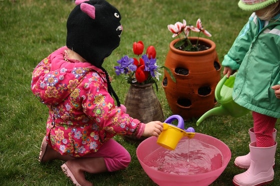 2 toddlers watering fake flowers outside with watering cans