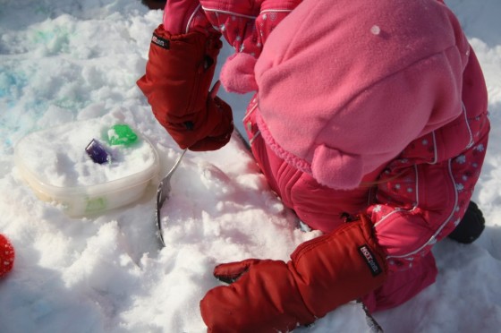 child digging in snow with spoon