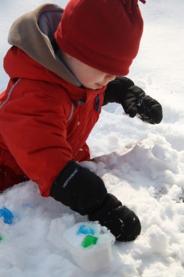 child playing with blue ice cubes in snow