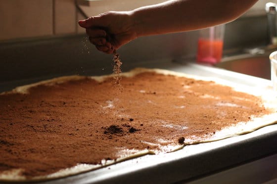 sprinkling cinnamon and sugar over rolled out dough