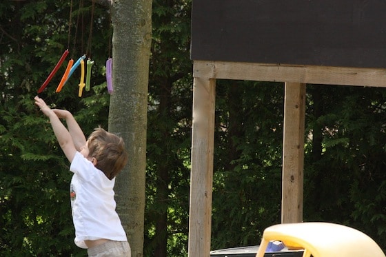 child batting at wind chimes beside playhouse