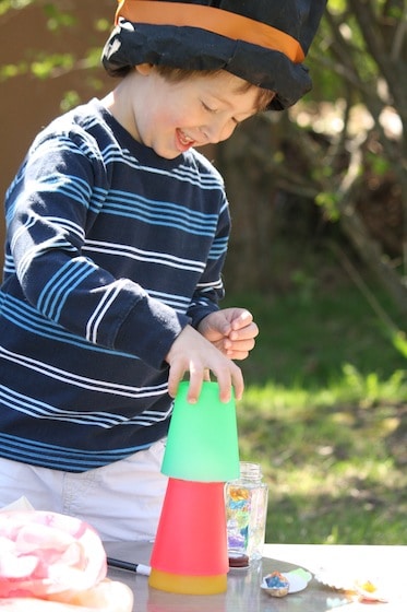 preschooler wearing homemade magician hat, doing magic trick with cups