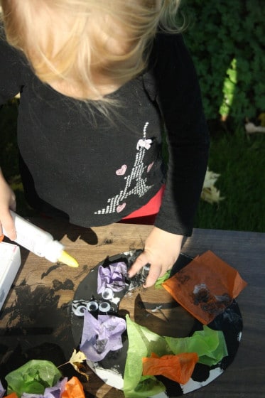 toddler gluing tissue paper to halloween wreath