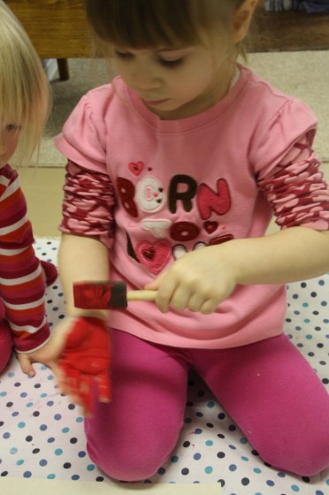 toddlers painting their hands red with sponge paintbrush