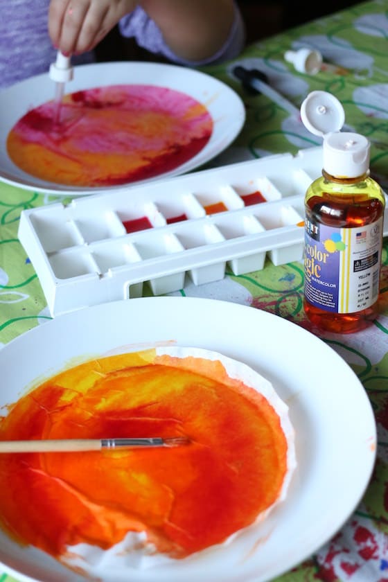 painted orange coffee filter beside ice cube tray filled with yellow red and orange liquid watercolours