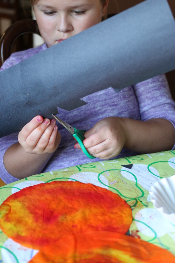 child cutting pumpkin eyes and mouth out of black construction paper