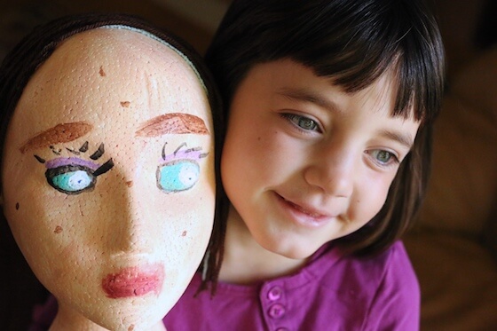 Girl holding styrofoam mannequin head painted as self-portrait