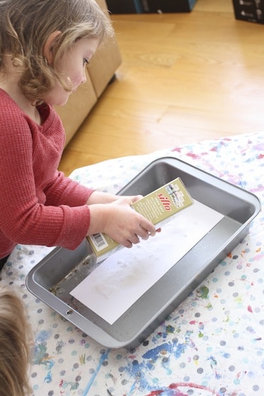 child pours salt over glue letters