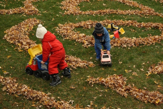 kids pushing toy trucks through roads made in leaves