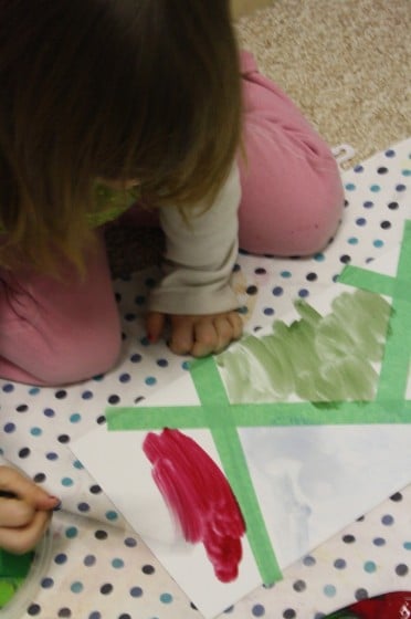 Toddler filling in sections of tape resist with watercolour paints