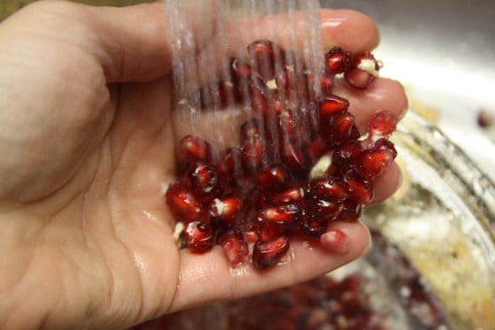 hand holding pomegranate seeds under running water