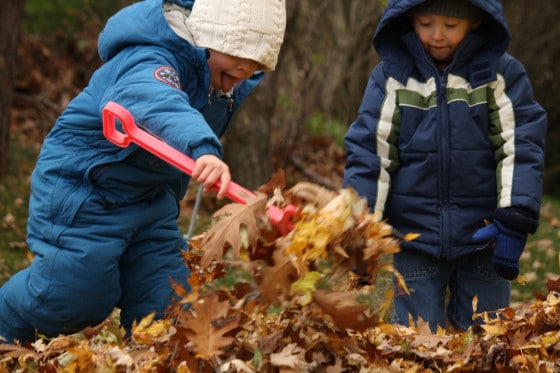 boy in blue snow suit adding leaves to pile at bottom of slide