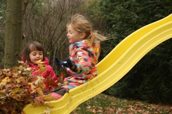 preschool girl sliding down slide into pile of leaves