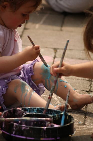 Toddler painting her legs with sidewalk paint