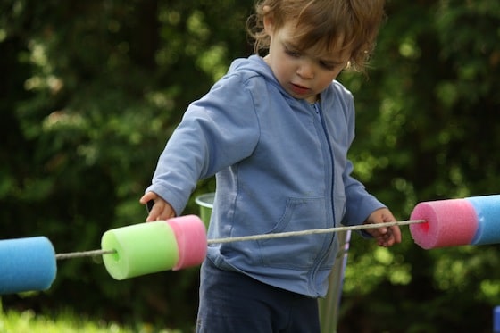 toddler playing with cut up pool noodles on rope