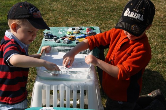 toddler and preschooler rinsing toy cars in pan of water