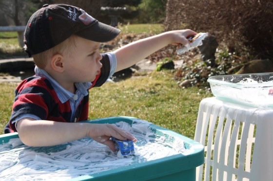 toddler putting car covered in shaving cream in water