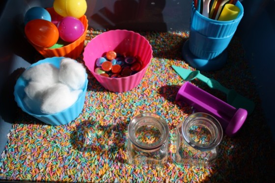 Sensory bin with coloured rice, jars, plastic eggs and glass beads