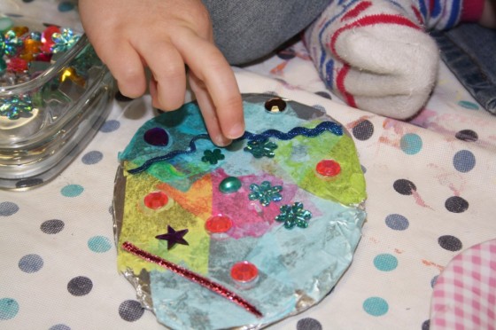 preschooler gluing gems on tin foil egg ornament