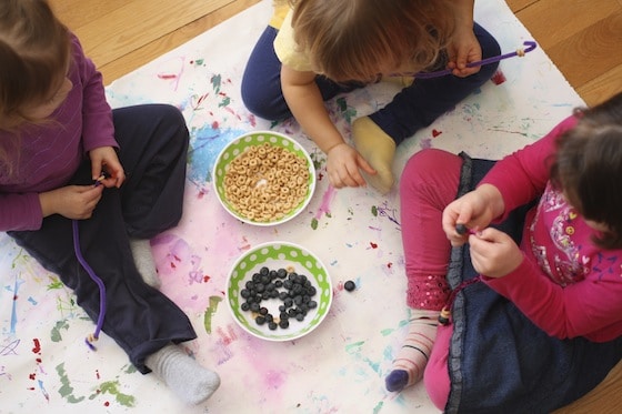 Gathered around a bowl, making bird feeders with cheerios and blueberries 