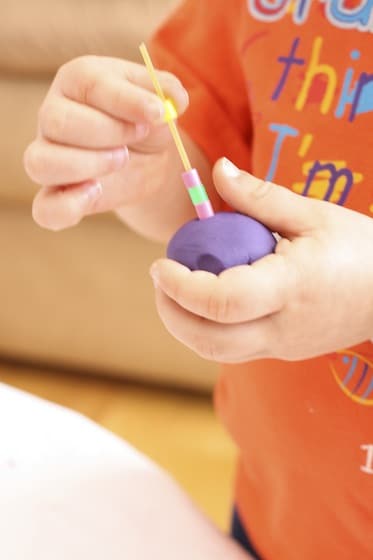 toddler threading beads onto spaghetti stuck into a ball of playdough