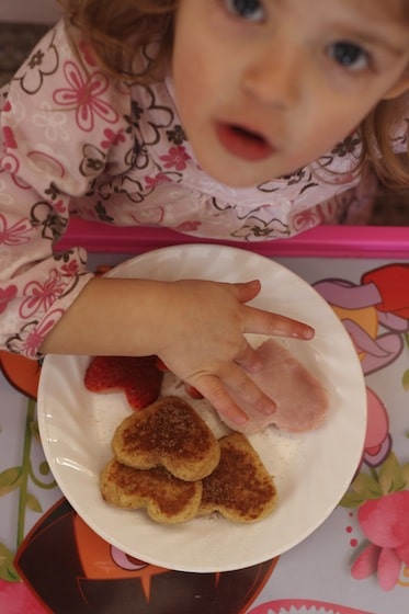 Child eating heart shaped French toast, ham and strawberries for lunch.