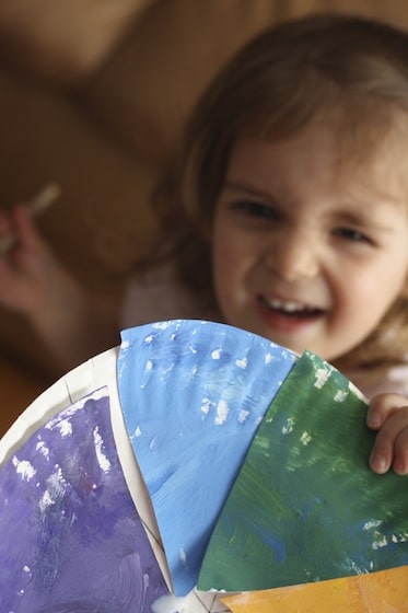 Toddler holding a paper plate colour wheel.