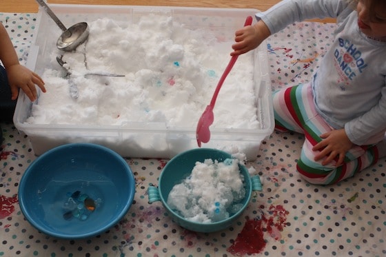 scooping snow out of the sensory bin and into bowls of water