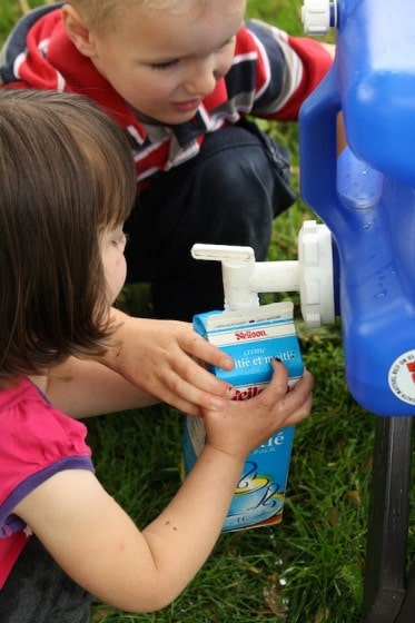 Kids filling empty milk carton with water from blue water carrier