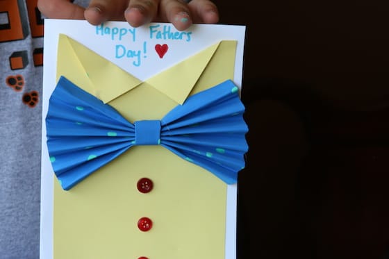 Kid holding yellow shirt and bow tie card
