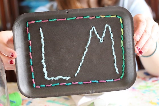 kid practing sewing initials on black styrofoam tray